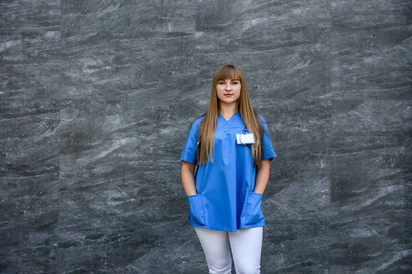 Beautiful nurse in blue uniform on gray background. Medical concept.