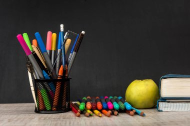 Kara tahtaya karşı bir yığın kitap ve malzeme içeren yeşil elma. Eğitim kavramı