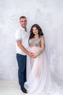 Pencerenin yanındaki stüdyoda poz veren inanılmaz çekici ve hamile çift.