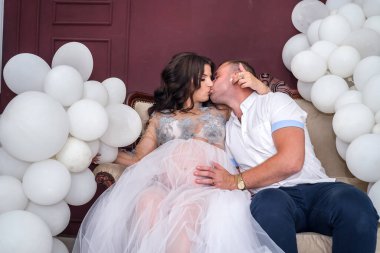 Stüdyoda kanepede oturup öpüşen hamile bir çift.