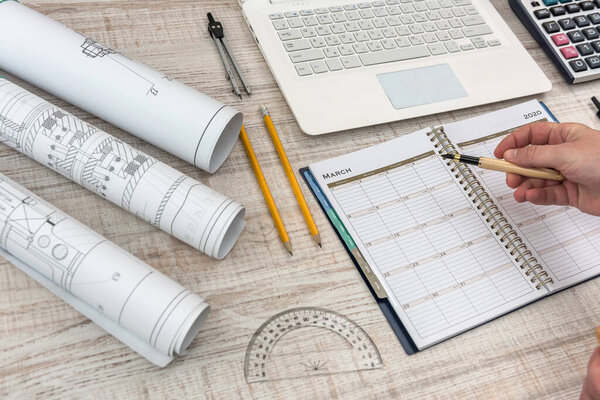 Male hands writing on notepad with part of industrial blueprint with calculator, tools and laptop.