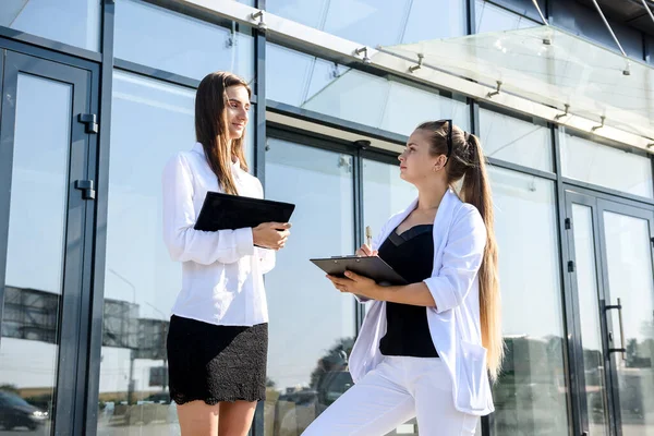 Two business women signing contract outdoors before building of big office center