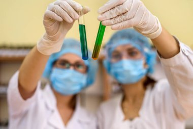 Kimyasal deney. Laboratuvarda test tüpleri olan koruyucu üniformalı iki kadın.