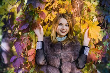 Moda kadını. Sonbahar parkında ağaçlar ve sarmaşıklarla poz veren kürklü kız.