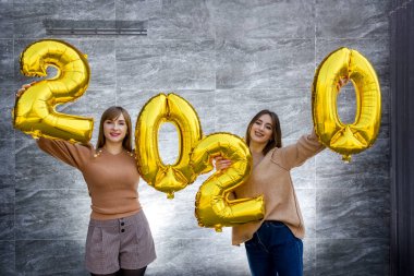 Kardeşler 2020 yılını kutluyorlar. Parti kutlamalarında altın hava balonları tutuyorlar.