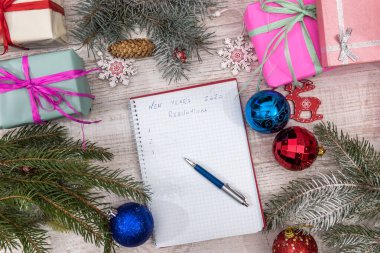 Not defterinde renkli toplar ve ahşap masada hediye kutuları olan yeni yıl kararları