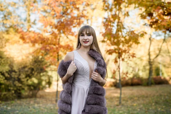 穿着时髦米色衣服和毛皮外套的女人在秋天的风景中摆姿势 流行服装 — 图库照片