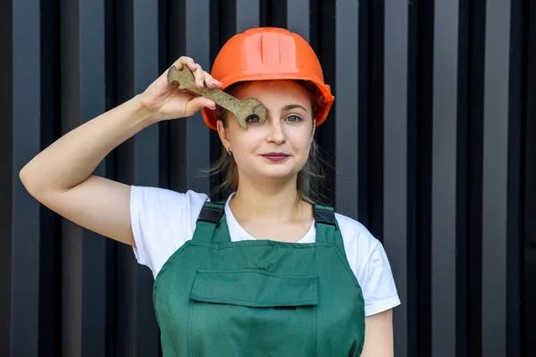 stock image Beautiful woman in helmet and coverall holding fixing key over eye