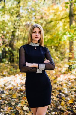 Sonbahar parkında bir bayan porteait. Siyah elbiseli güzel kadın sarı ağaçlarla poz veriyor.