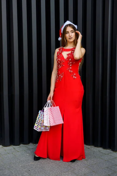 赤いドレスのきれいな女性がギフトバッグを保持 新年とクリスマスプレゼントのコンセプト — ストック写真