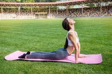 Paspasın üzerindeki kadın yeşil çimlerde sabah egzersizi yapıyor.