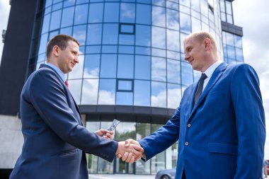 Takım elbiseli iki adam karşı binada el sıkışıyor.