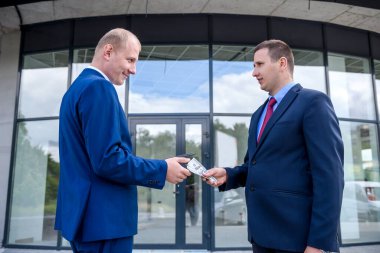 Takım elbiseli bir işadamı bir başkasına dolar banknotları veriyor.