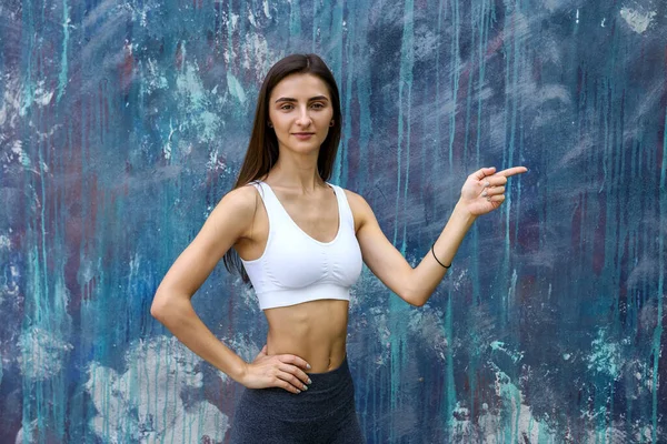 穿着运动服的年轻女子在灰色的墙壁上做手势 — 图库照片
