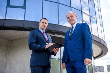 İki ciddi iş adamı iş merkezine karşı poz veriyor.