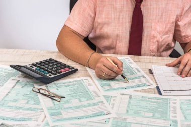 Man filling 1040 tax form at workplace. Performing tax calculations. Close up clipart
