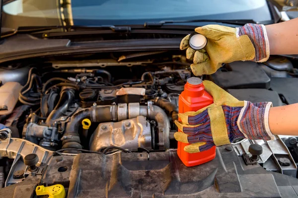 Oil change concept. Male hand in glove with oil bottle and car engine close up