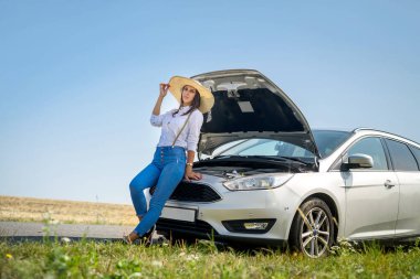 Stresli genç bir kadın arabasının motoruna bakıyor. Yolculuk sorunları. Arabanın tamire ihtiyacı var..