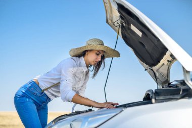 Stresli genç bir kadın arabasının motoruna bakıyor. Yolculuk sorunları. Arabanın tamire ihtiyacı var..