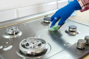 Sünger ve kauçuk eldivenli bir kadın fırın kapağını silmek için kullanılmış.