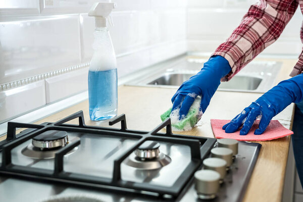 young woman cleaning in rubber gloves and sponge in the kitchen at home.