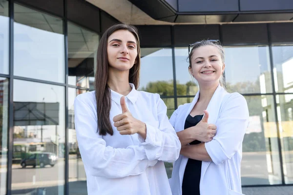 Happy women in business suits with folder standing before big business office