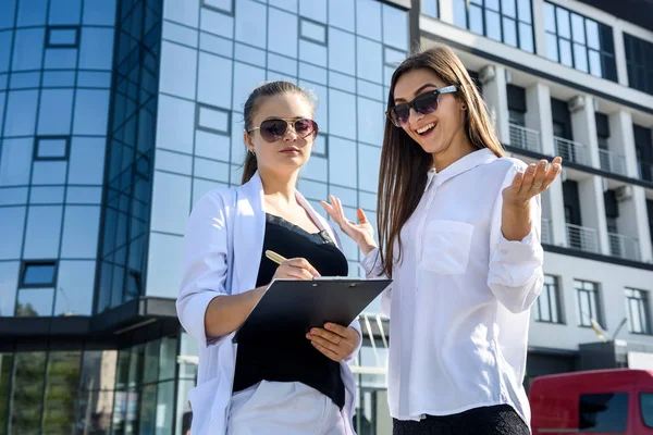 Two business women signing contract outdoors before building of big office center