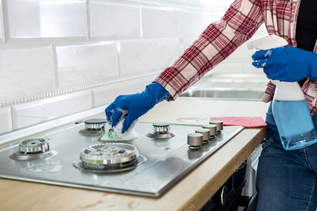 Woman cleaning stainless steel gas surface in the kitchen with rubber gloves.