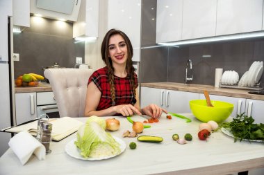 Mutfak masasında poz veren kız sağlıklı bir yaşam için farklı sebze ve sebzelerden oluşan bir salata hazırlıyor.