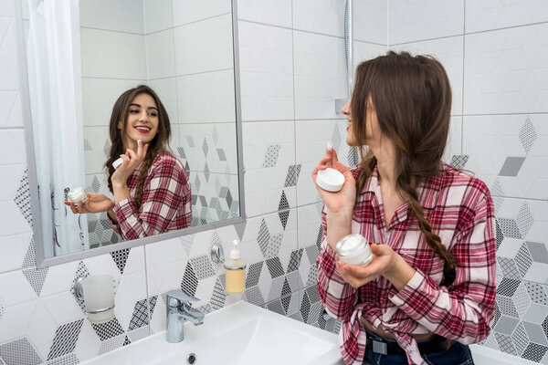 beautiful girl in the bathroom applies cream on her face. beauty concept.