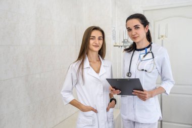 Genç ve kendinden emin gülümseyen doktorlar hastanede kamera önünde poz veriyorlar.