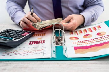 Ofiste çalışan bir iş adamı. Bir adam mal kiralamak ya da satmaktan kazanç elde ediyor. İş Analizi ve Strateji Konsepti. Masada dolar olan iş grafikleri ve belgeler.