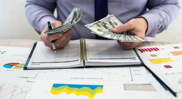 Businessman working in office. A man counts profits from renting or selling goods. Business Analysis and Strategy Concept. Business graphs and documents with dollars on the table.