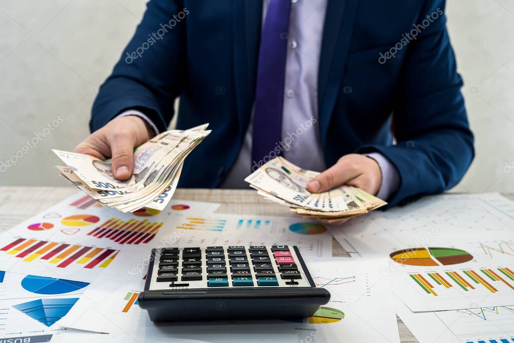 young businessman in suit counts hryvnia money and works with charts and documents as net monthly income. The concept of money is salary or corruption. Work in the office.