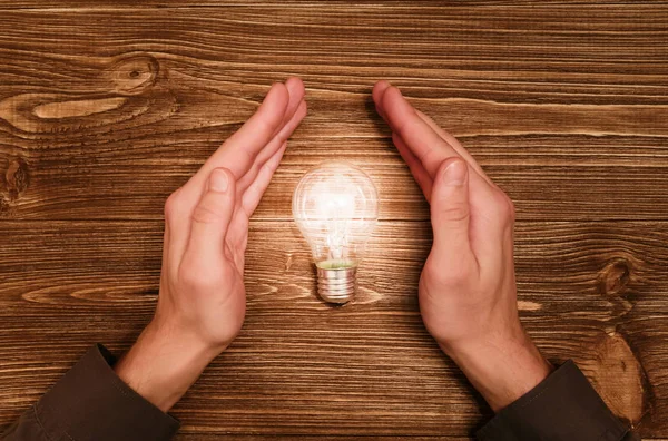Businessman hold in hands a great idea with light bulb on wooden background. Success, creativity and great idea concept