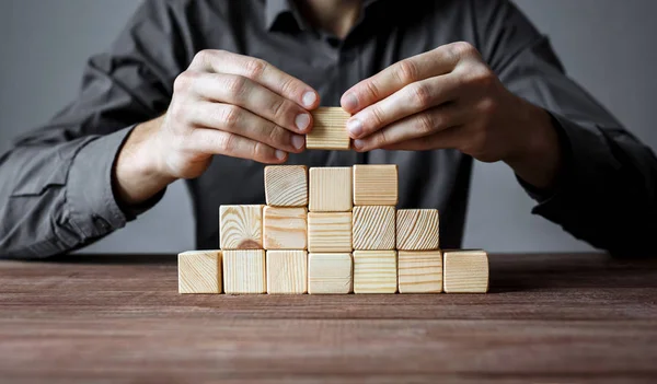 Uomo d'affari che costruisce una piramide di blocchi di legno. Concetto di gerarchia delle imprese e strategia aziendale . — Foto Stock