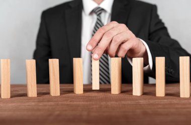 İşadamı, merkezi bir domino hattı üzerine tahta blok kuruyor. Risk ve iş stratejisi kavramı..