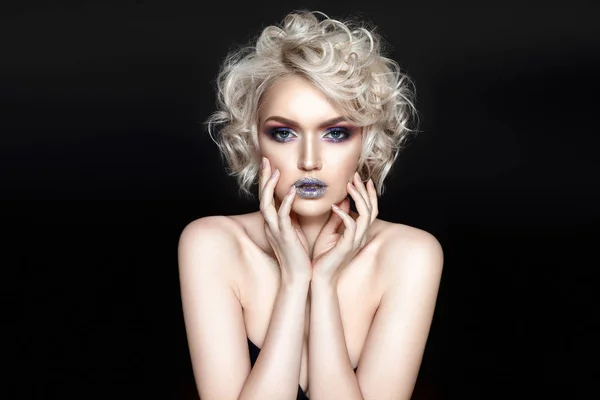 Young curly model with fashionable glossy makeup posing on black background