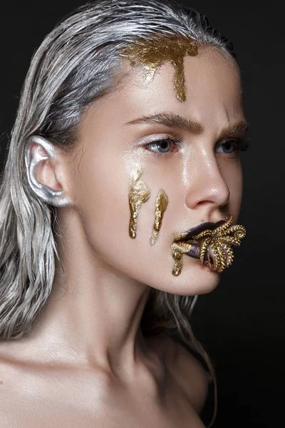 Fashion portrait of model with liquid gold on face and golden octopus in mouth