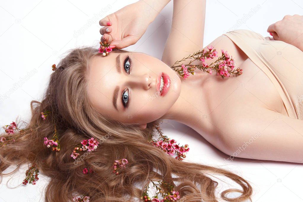 Portrait of young model with field flowers in wavy hair on white background