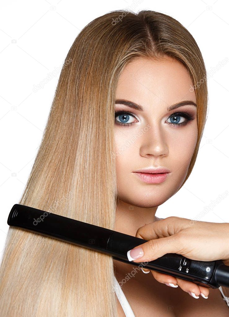 Portrait of young blonde woman with hair straightener on white background