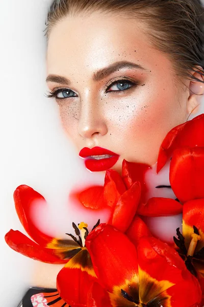 スタイリッシュな化粧品の白い液体に赤いチューリップとポーズで若いモデル — ストック写真