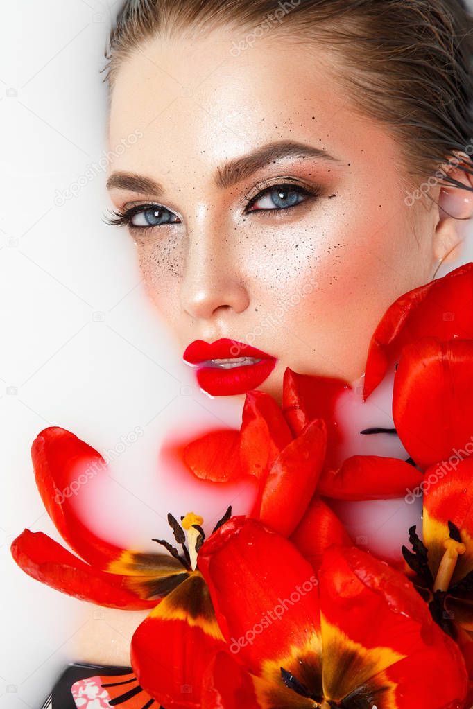 Young model with stylish makeup posing with red tulips in white liquid