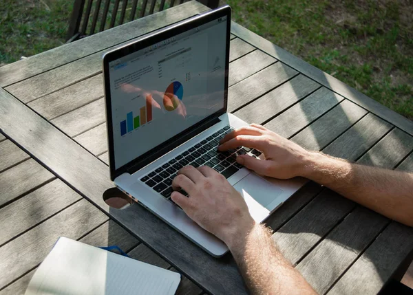 Ręce człowieka za pomocą laptopa z wykresu analitycznego na biurko w pracy w ogrodzie, na świeże powietrze, freelancer — Zdjęcie stockowe