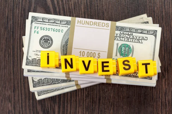 Investimentos conceituais, palavra feita por carta, pilha de notas de dólar — Fotografia de Stock