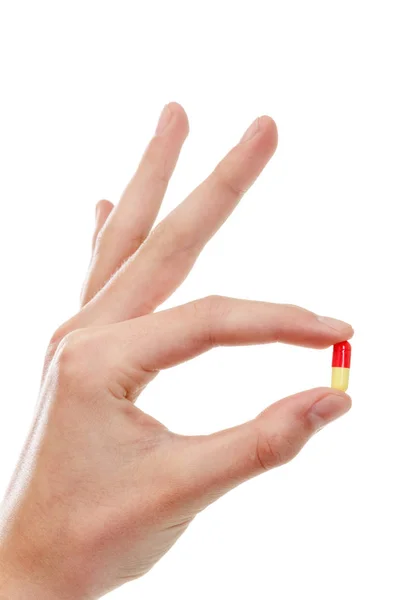 Mão segurando uma pílula entre polegar e indicador — Fotografia de Stock