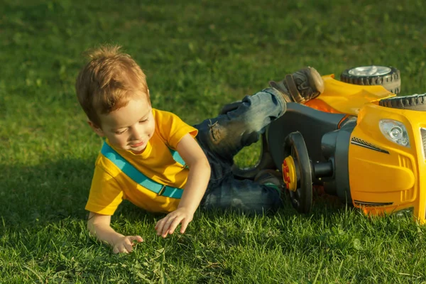 Lindo niño positivo, jugando felizmente con el coche bebé en el prado verde —  Fotos de Stock