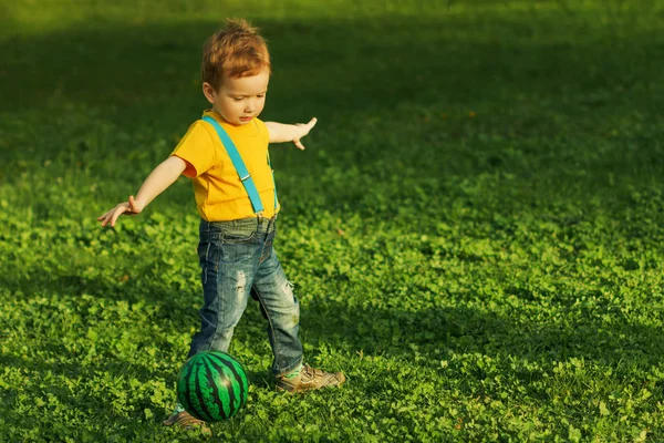 Lindo niño positivo, jugando felizmente con la pelota en el prado verde —  Fotos de Stock