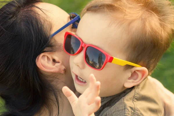 El hijo besa y abraza a su madre en gafas de sol al aire libre . — Foto de Stock
