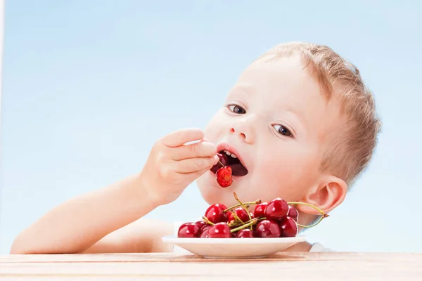 Дитина з червоними ягодами, хлопчик їсть і вибирає вишню . — стокове фото